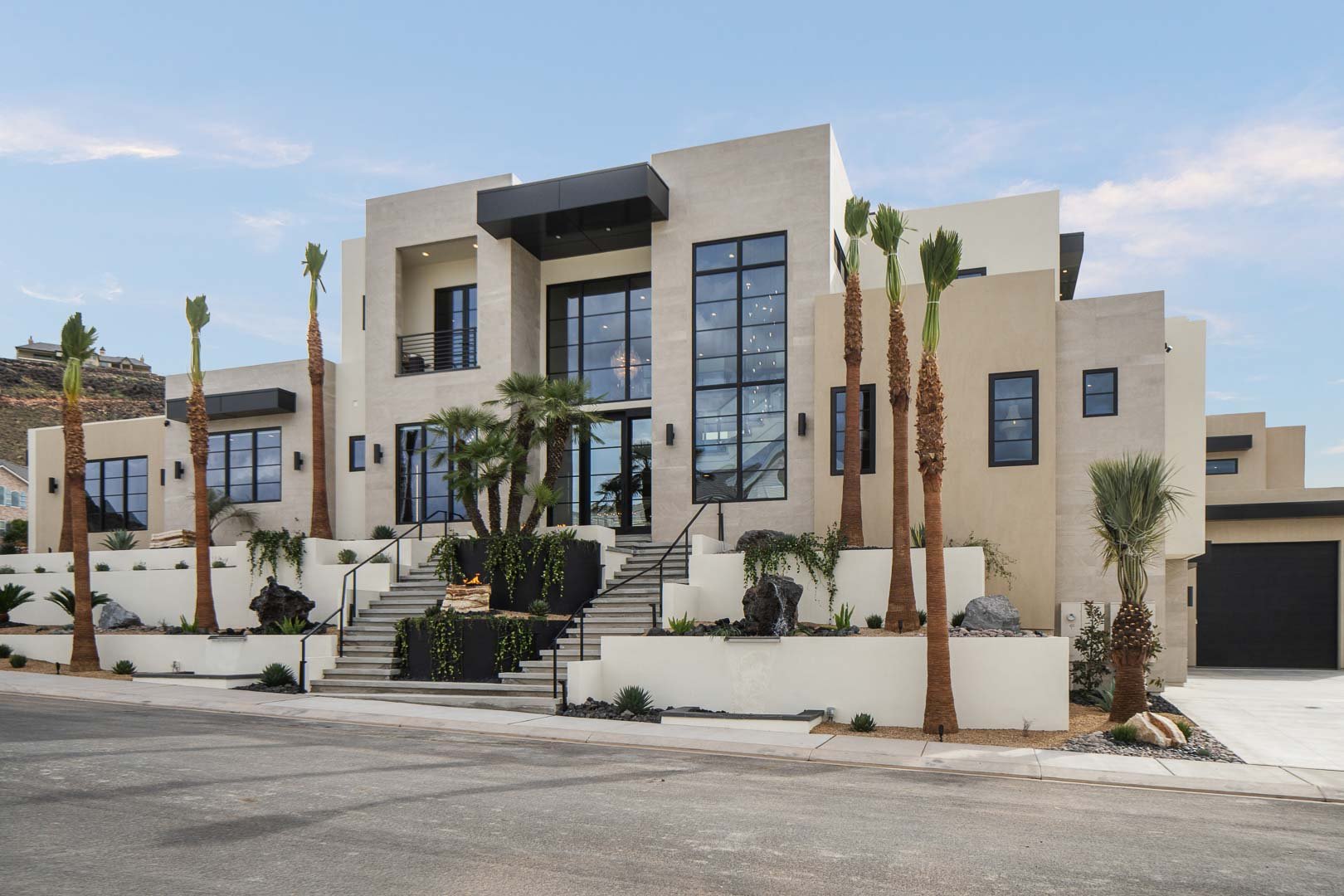 Chateau du Soleil completed exterior — terraced stucco, black-framed windows, desert landscaping with volcanic rock, fire feature on entry stairs.